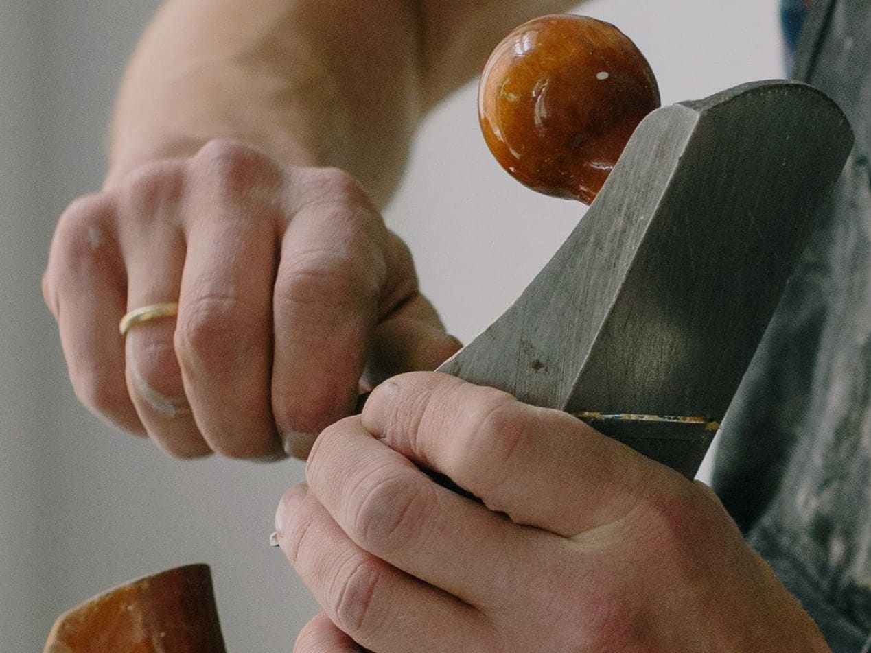Les mains d’un menuisier en tablier de travail règlent la lame d’un rabot à main