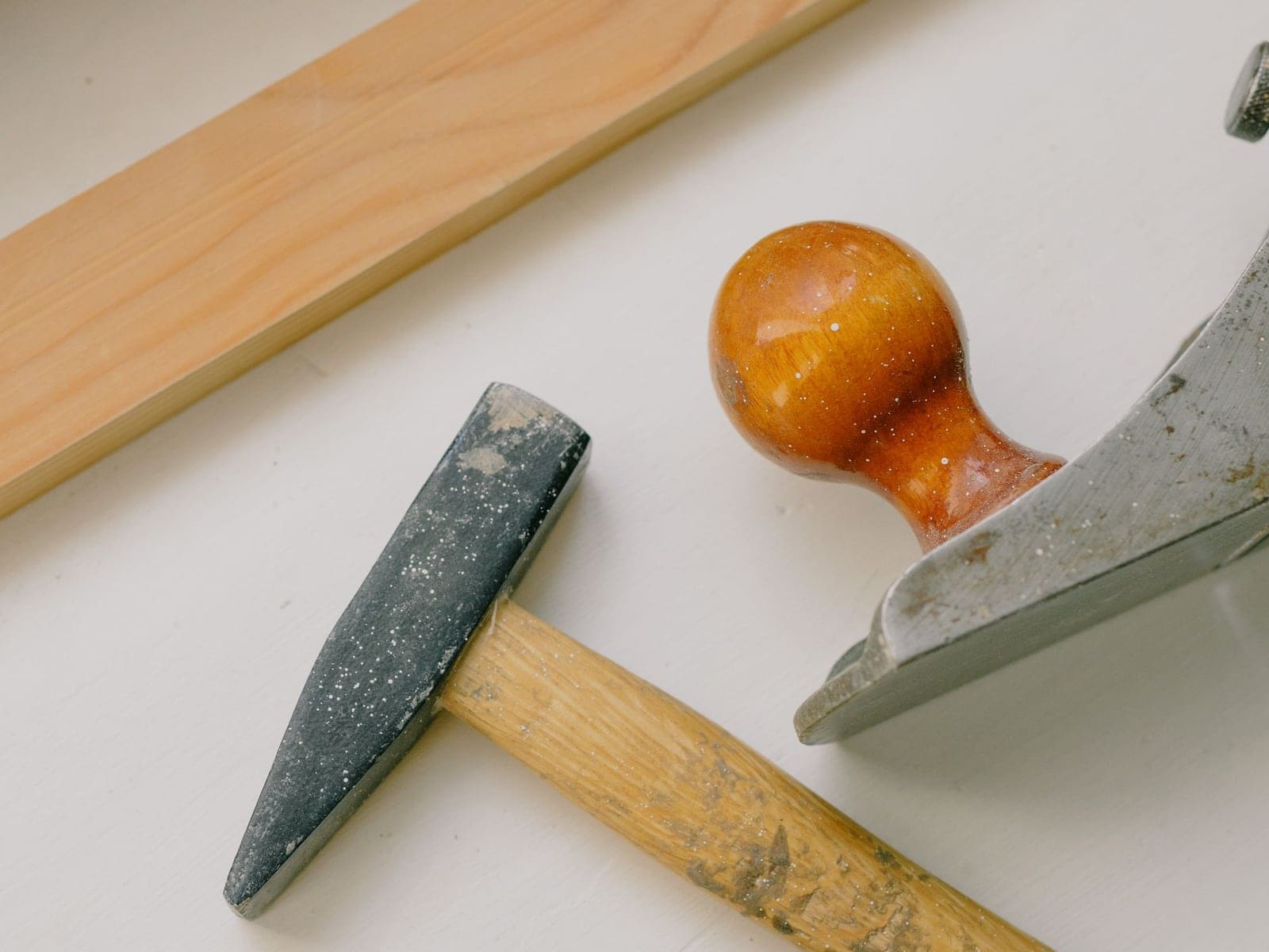 Une planche de sapin, un marteau de menuisier et un rabot posés sur un appui de fenêtre blanc