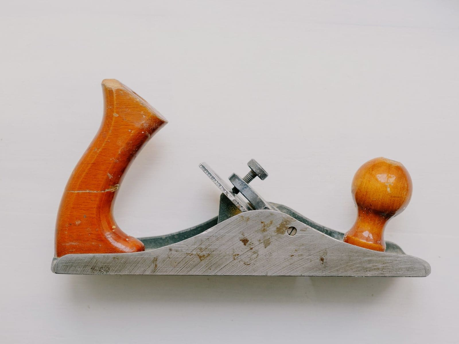 Un rabot à main ancien, poignée et bouton en bois, posé sur un fond blanc
