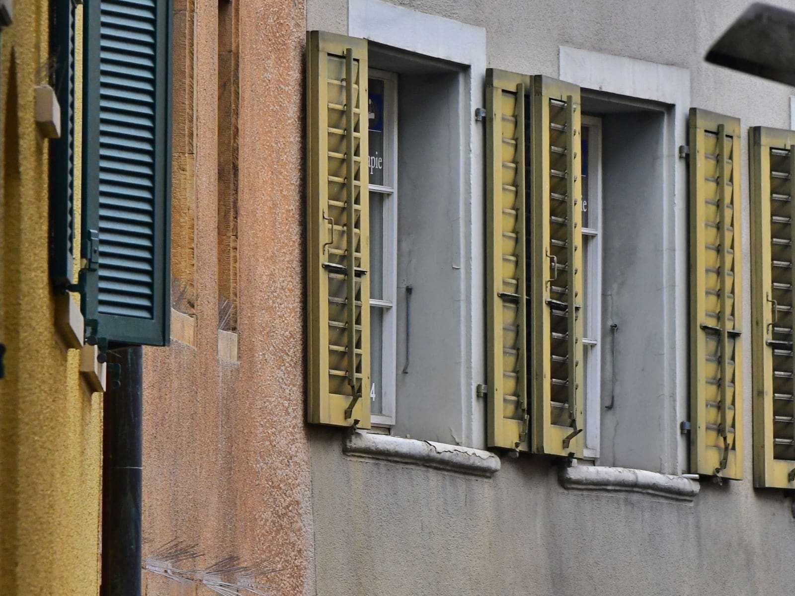 Façade ancienne d’une rue de vieille ville, volets en bois à lames peints en vert, en jaune et en mauve